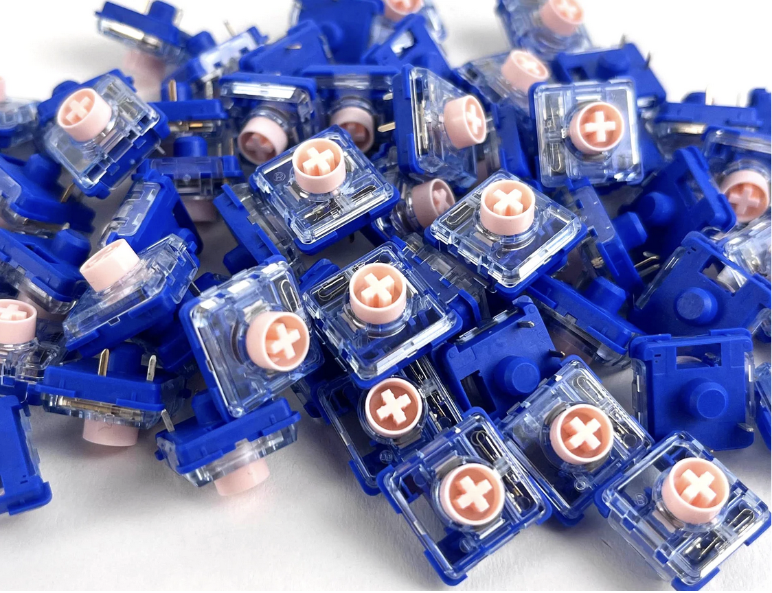 A bunch of Kailh V2 Pink Islands low profile switches. The stems are a light pastel pink, clear upper housing and deep navy blue housing base. 